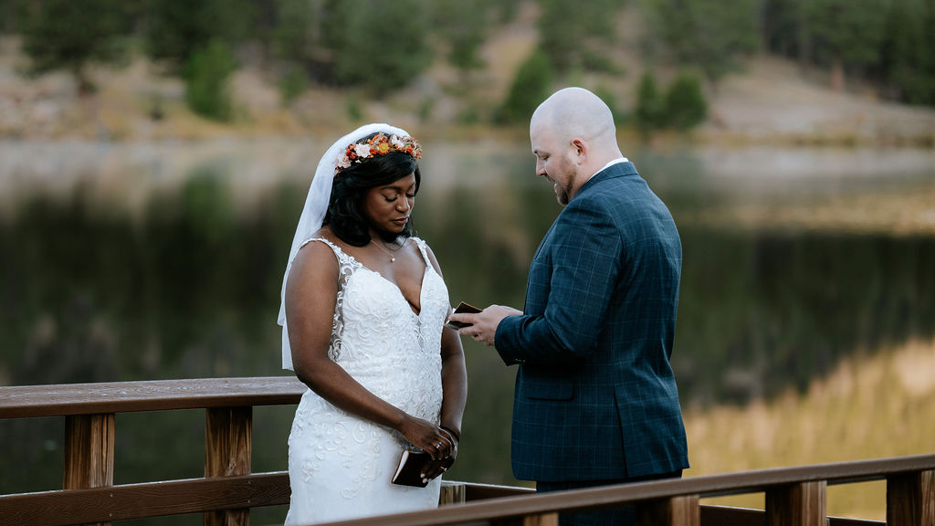 A bride cries while standing on a boardwalk overlook as her groom reads her his vows from a leather book during their crested butte elopement