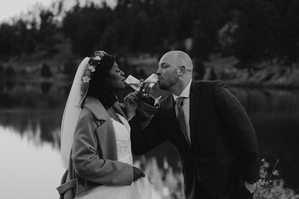 Newlyweds share champagne while standing by a lake