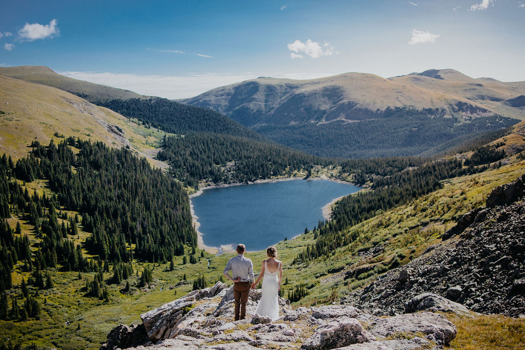 Newlyweds hold hands on a rocky mountain trail while taking in the incredible scenery