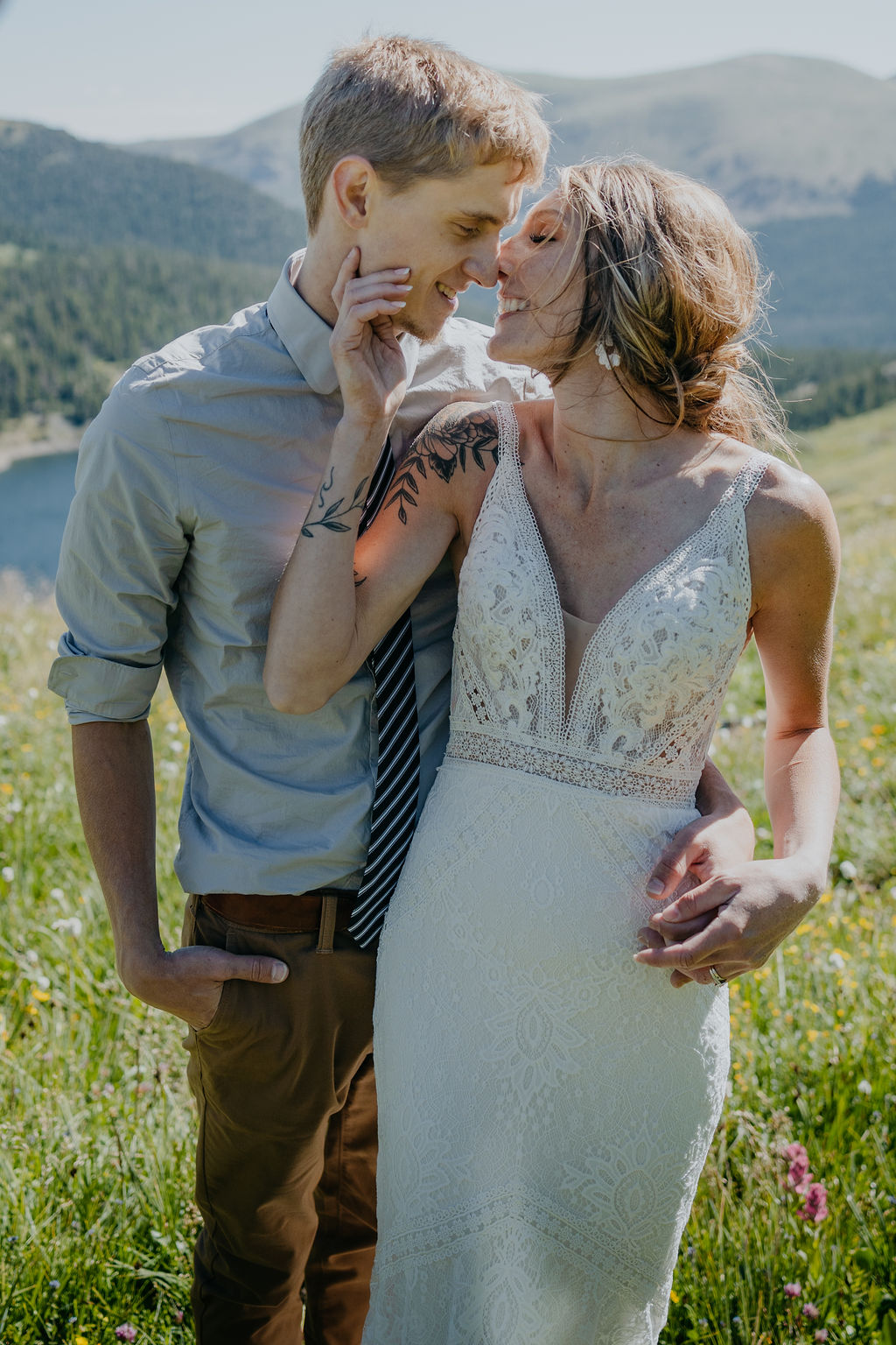 A bride leans back to kiss her groom while standing in a wildflower meadow overlooking a mountain lake during their denver elopement