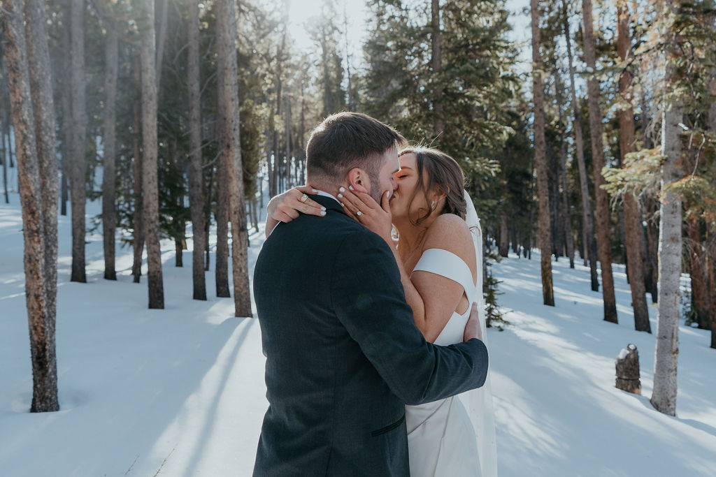 Newlyweds kiss in a snow covered forest at sunset