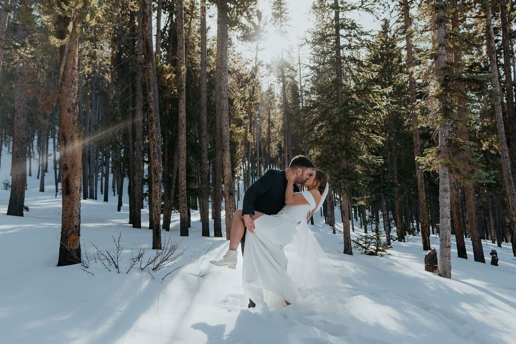 A groom holds the leg and dips his bride in a snowy forest at sunset during their san juan mountains elopement