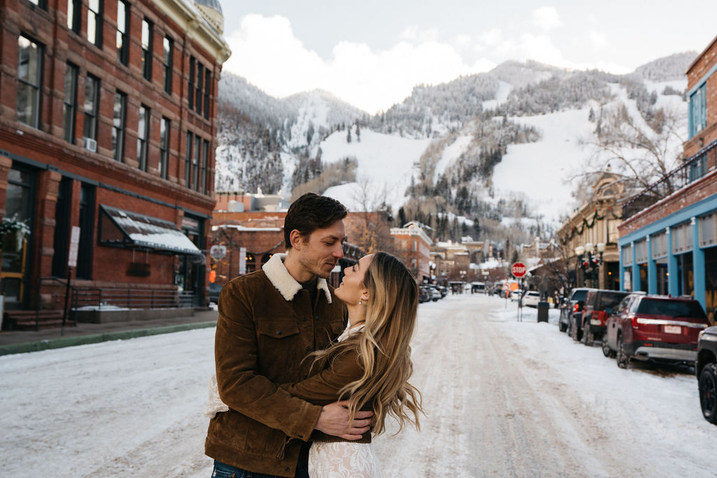 Newlyweds kiss while standing in a snowy downtown road during their aspen elopement