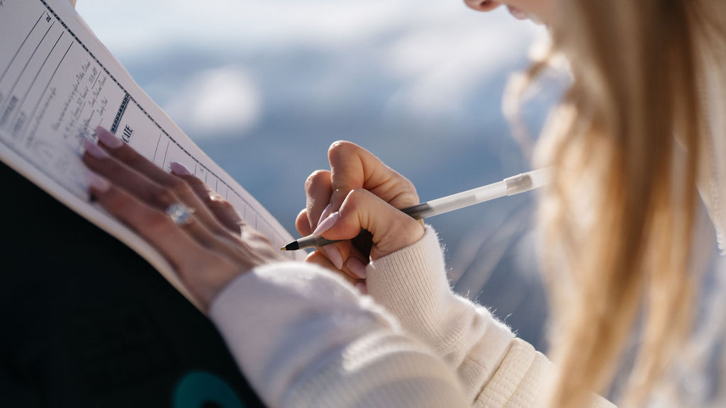 A bride signs her wedding certificate on a snowy mountain