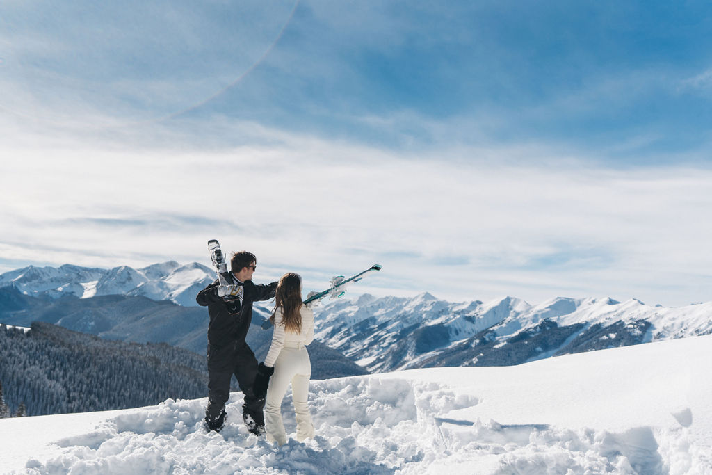 Newlyweds hold their skis while looking out to the snow covered mountains during their aspen elopement