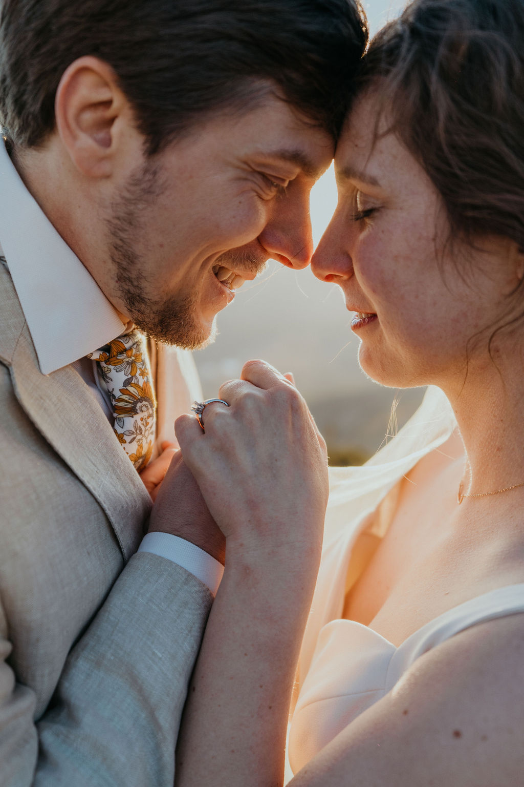 Newlyweds hold hands and touch foreheads at sunset during their elopement