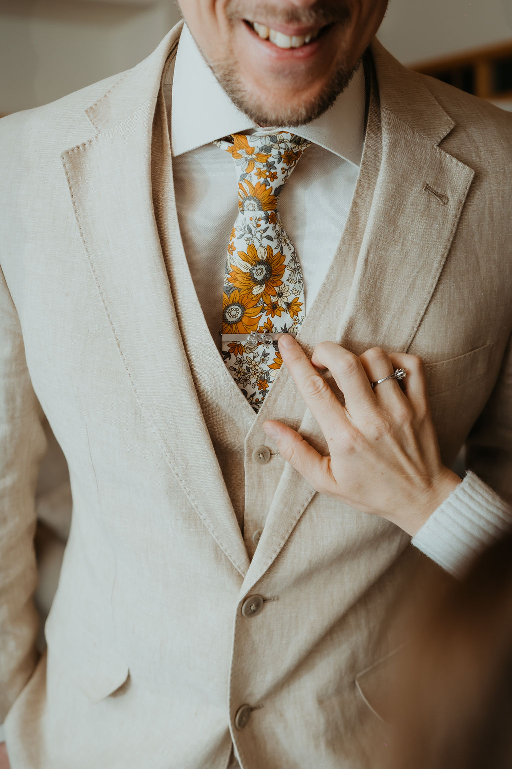 A groom shows off his colorful floral print tie and tie clip in his tan suit during his estes park elopement