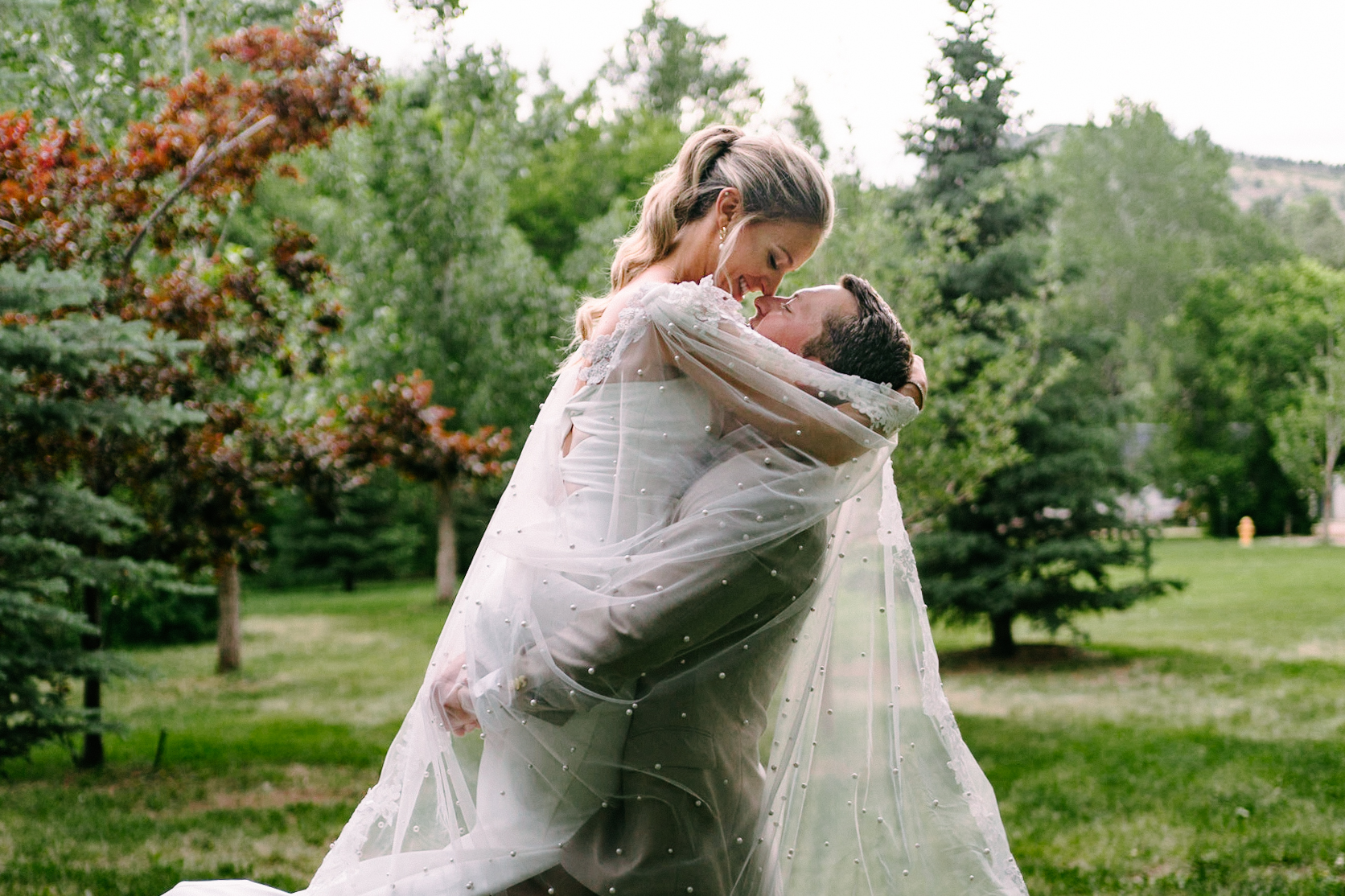 Newlyweds kiss in a garden with the veil flowing in the wind behind them