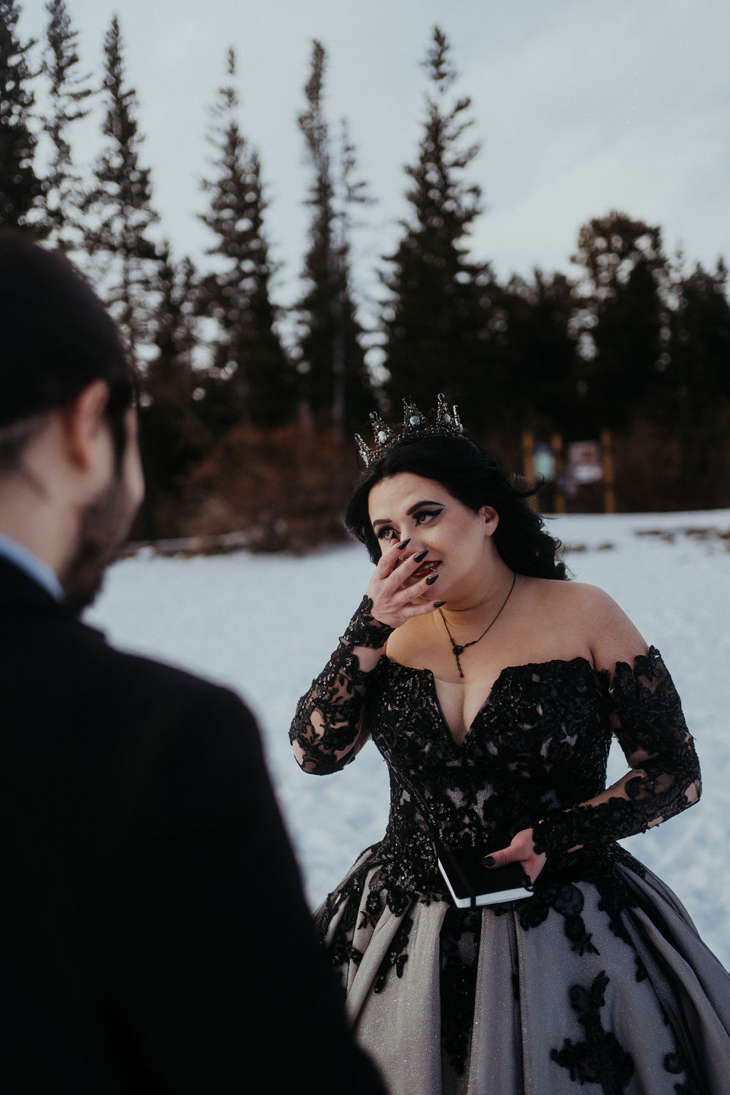 A bride in a black lace dress cries during the vows of her snowy telluride elopement