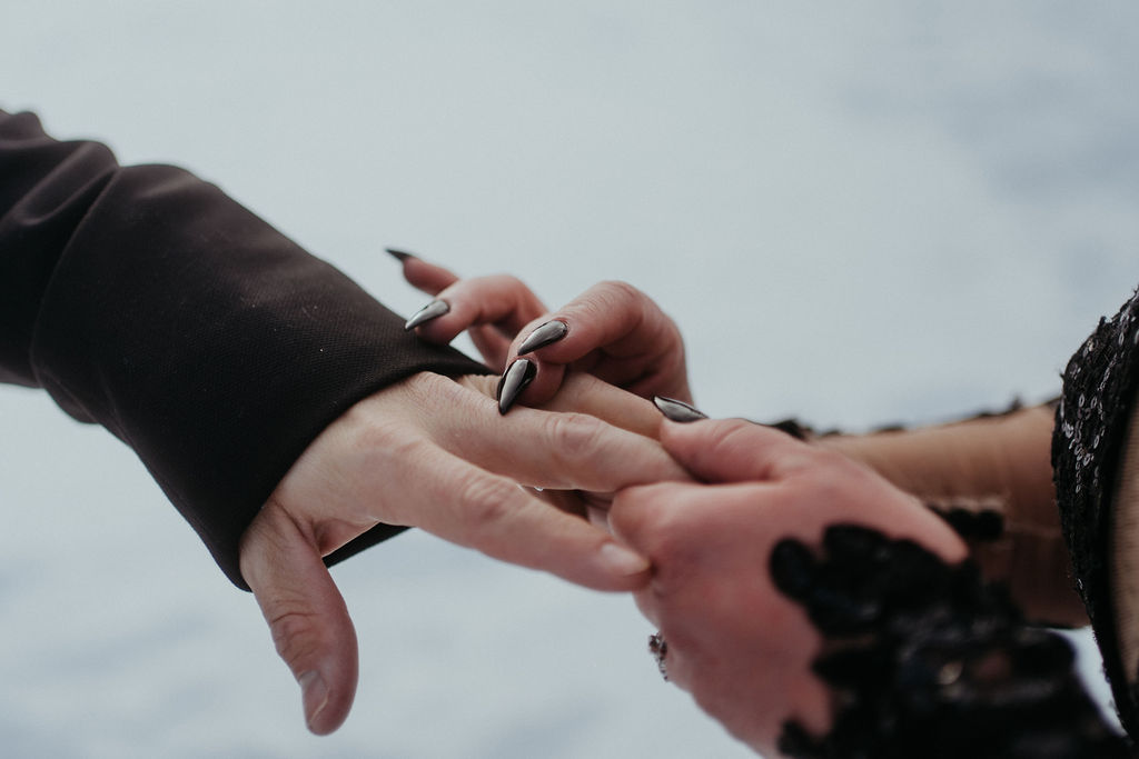 Details of a bride in a black dress with black nails putting the ring on her husband at their telluride elopement