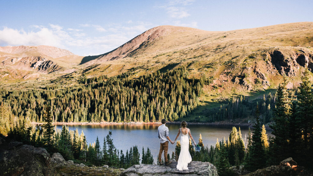 Newly weds stand on rock overlooking the colorado mountains on their elopement day