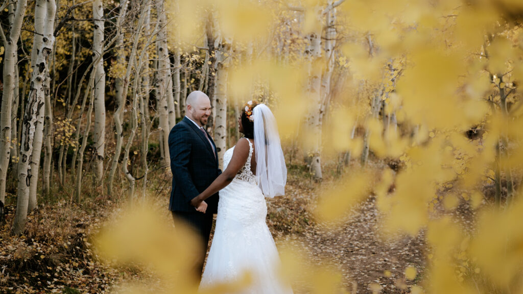 Newlyweds smile and embrace in a fall forest trail during their Rocky mountain elopeemnt